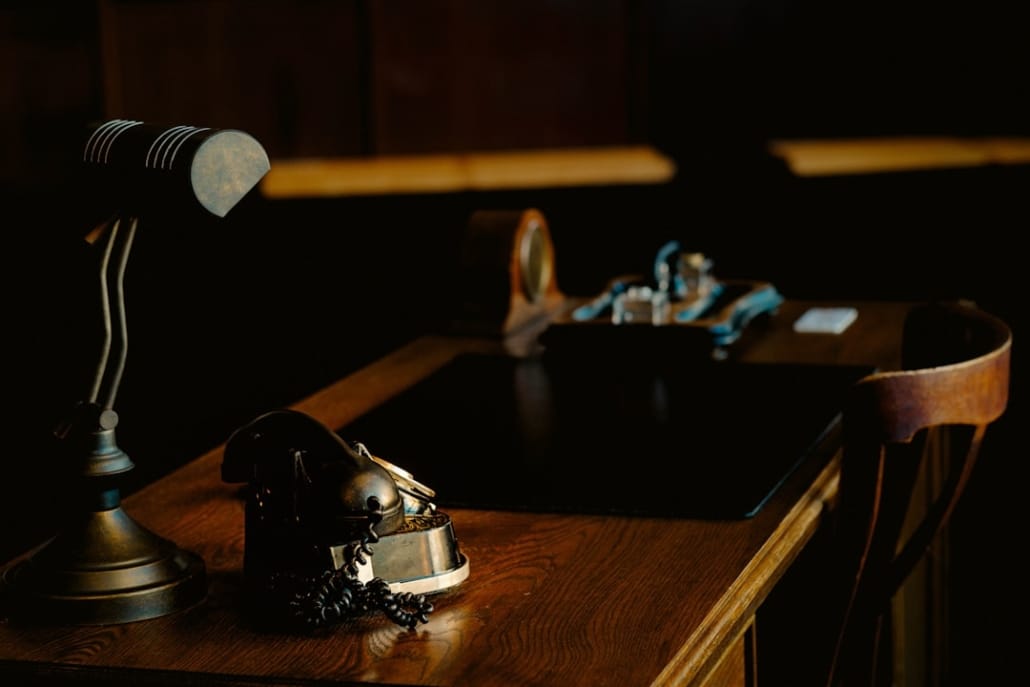 Bureau de travail sobre et raffiné, documents financiers ou juridiques posés sur un bureau en bois sombre ou pierre naturelle, lumière naturelle latérale tamisée, atmosphère de réflexion et de décision stratégique — aucun visage identifiable ou en arrière-plan flou, ancrage possible dans un environnement architectural marocain moderne ou un bureau premium nord-africain.