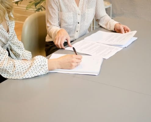 Deux personnes en réunion de travail concentrées sur des documents chiffrés ou un écran d'analyse financière, sans sourire forcé, ambiance sérieuse et confidentielle. Tenue professionnelle, bureau sobre et moderne.